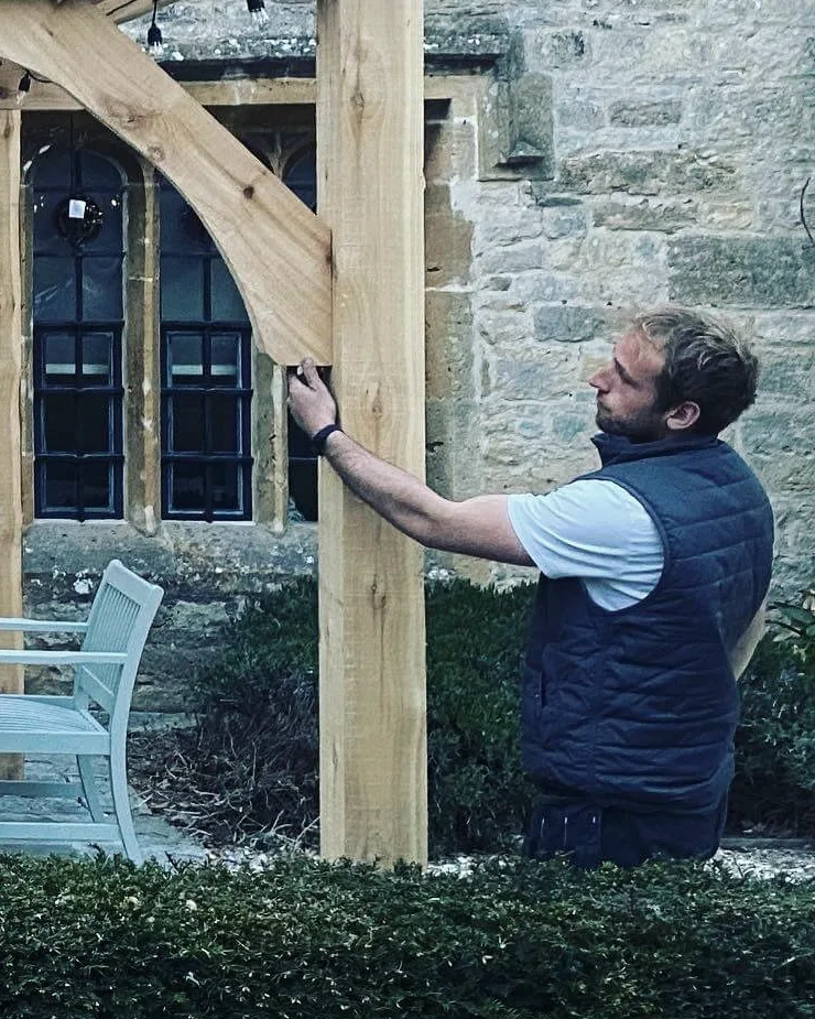 Harvey Jameson fitting an oak pergola beside a Cotswold stone building