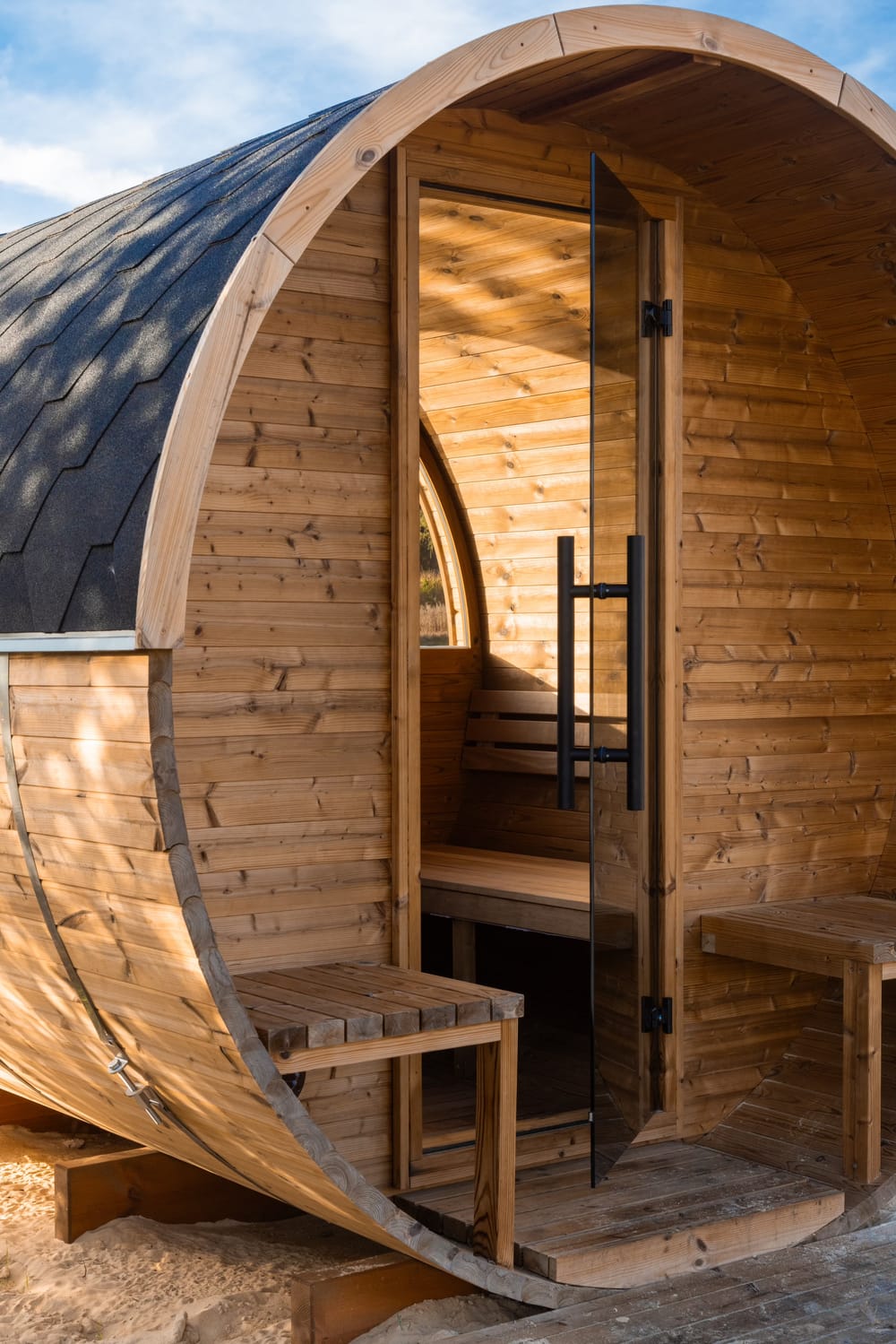 The round front of the barrel sauna close up, with its glass door, black handle and two timber seats