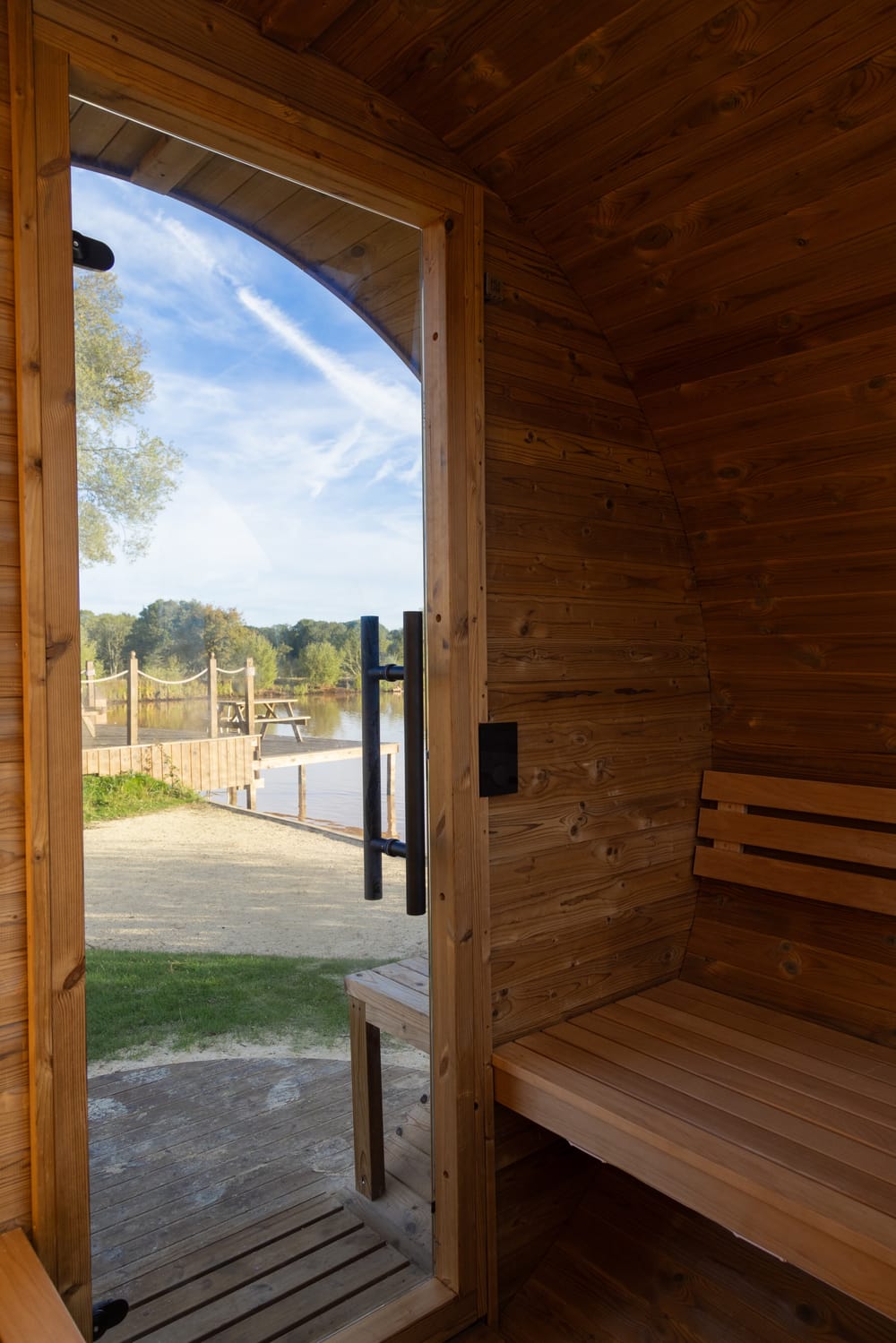 Looking out through the sauna's open glass door to a path and a jetty on the water